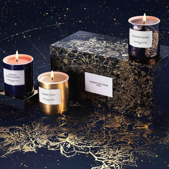 Close-up of Dior scented candles: Ambre Nuit in gold, 30 Montaigne in patterned black, and Jardin d’Orangers in classic black containers