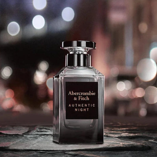 Abercrombie & Fitch Authentic Night perfume bottle displayed on a dark stone surface with a blurred city lights bokeh background.
