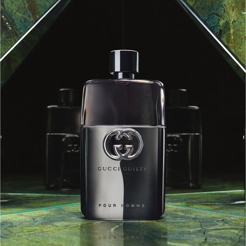 Gucci Guilty Pour Homme perfume bottle on a reflective surface with a dark background