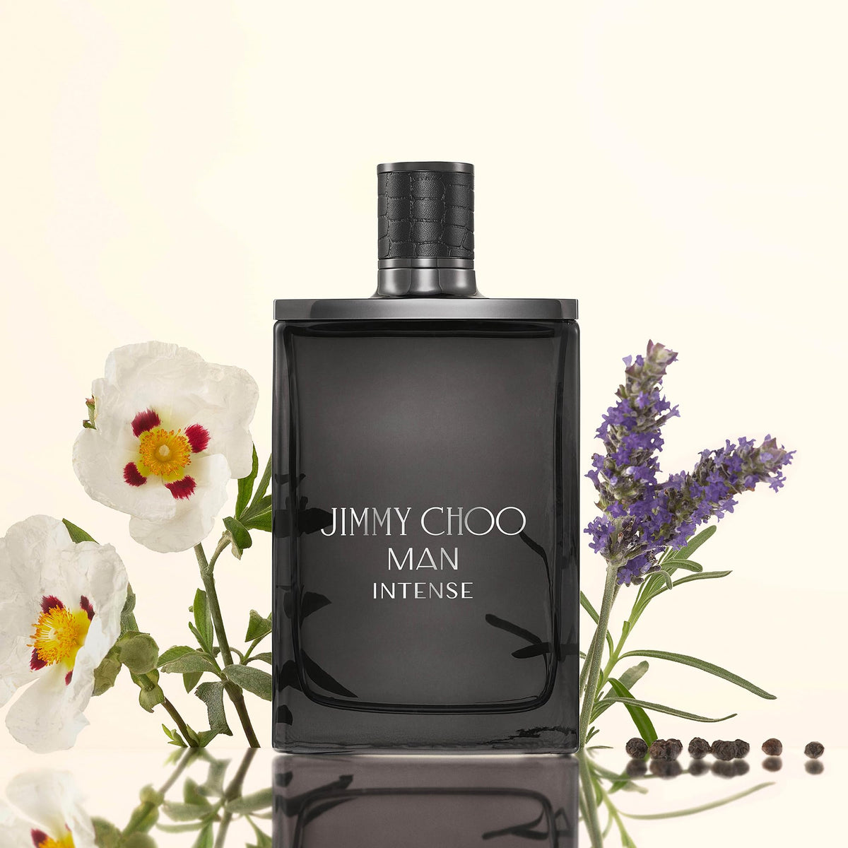 Jimmy Choo Man Intense perfume bottle in a dark smoky glass, styled with white flowers and purple lavender sprigs on a light cream background.