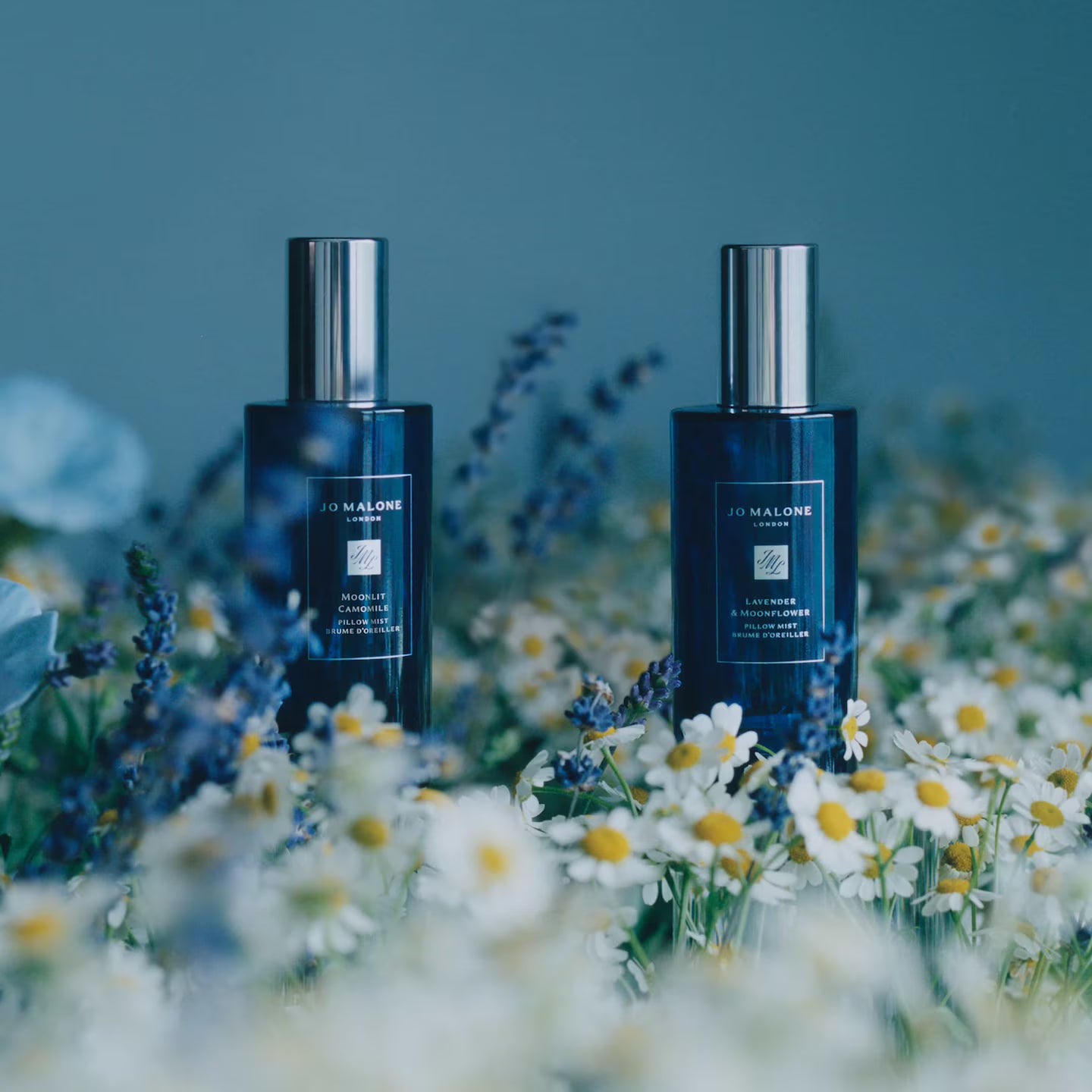 Two Jo Malone bottles surrounded by flowers on a blurred natural background