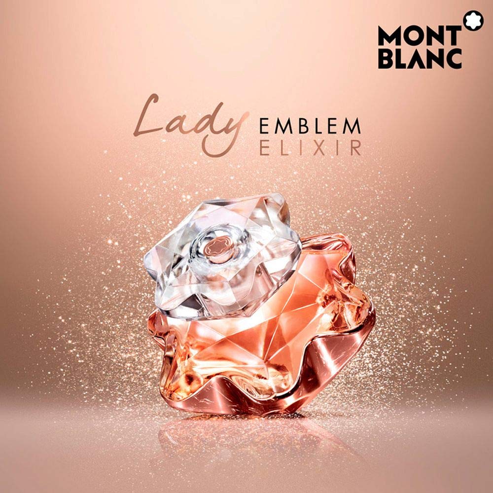 Mont Blanc Lady Emblem Elixir perfume bottle with a faceted rose design in rose gold and clear glass, set against a warm peach background with brand text and sparkles.