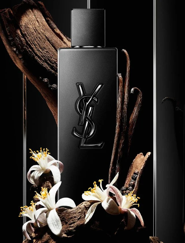 Black YSL perfume bottle with vanilla beans and flowers on a dark background