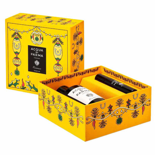 A yellow Acqua di Parma gift box shown closed and open, with two bottles of fragrance placed inside. The packaging features decorative botanical and holiday-style illustrations in black, green, and red, with a black brand panel on the front.