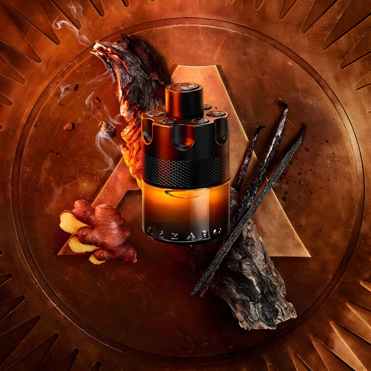An AZZARO fragrance bottle with a black cap and amber-to-orange gradient glass, styled on a metallic bronze circular plate with ginger, vanilla beans, and a piece of wood.