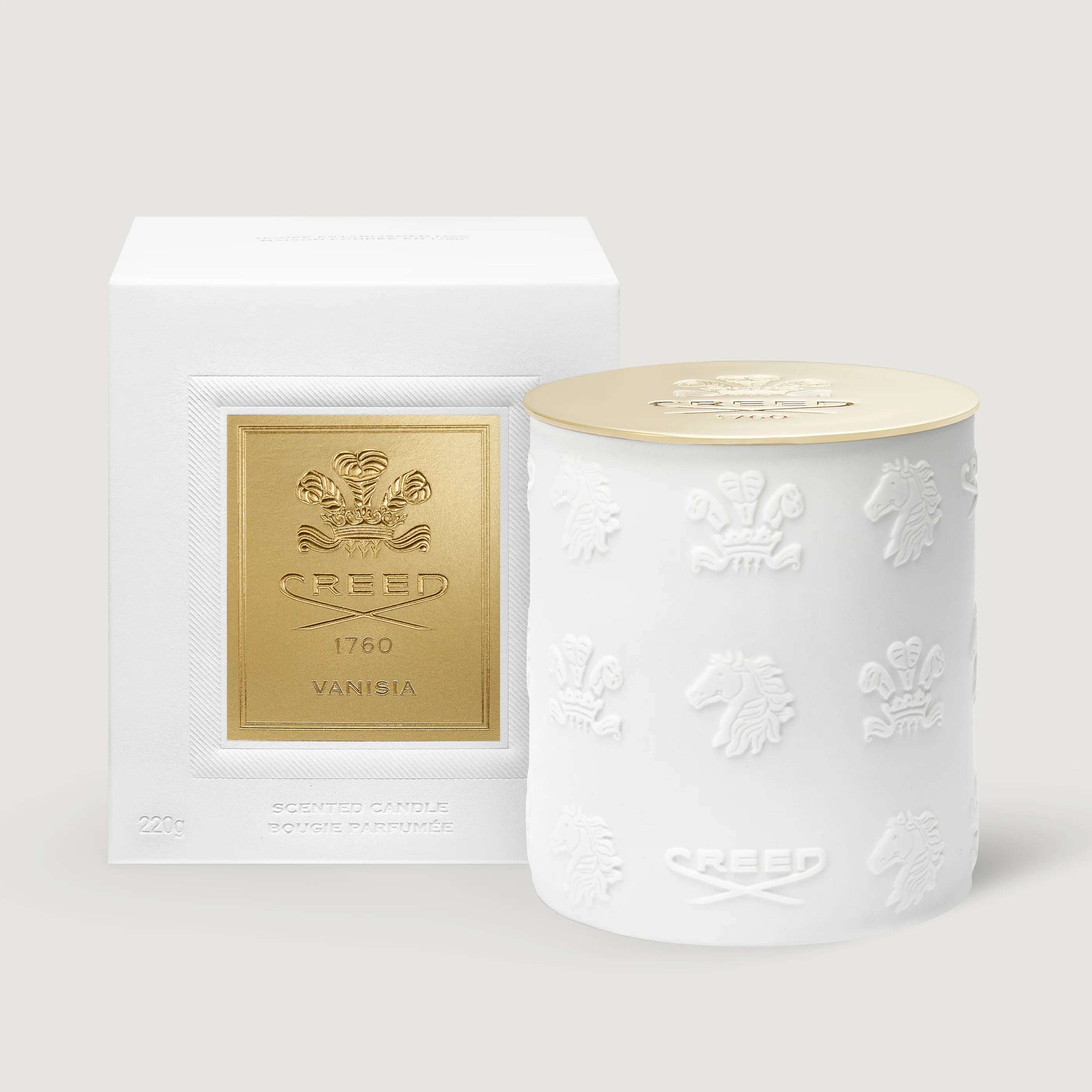A white ceramic candle jar with embossed crest motifs and a gold lid, shown next to its white box packaging featuring a gold crest label. The brand name 'Creed' is visible on both the box and the jar.