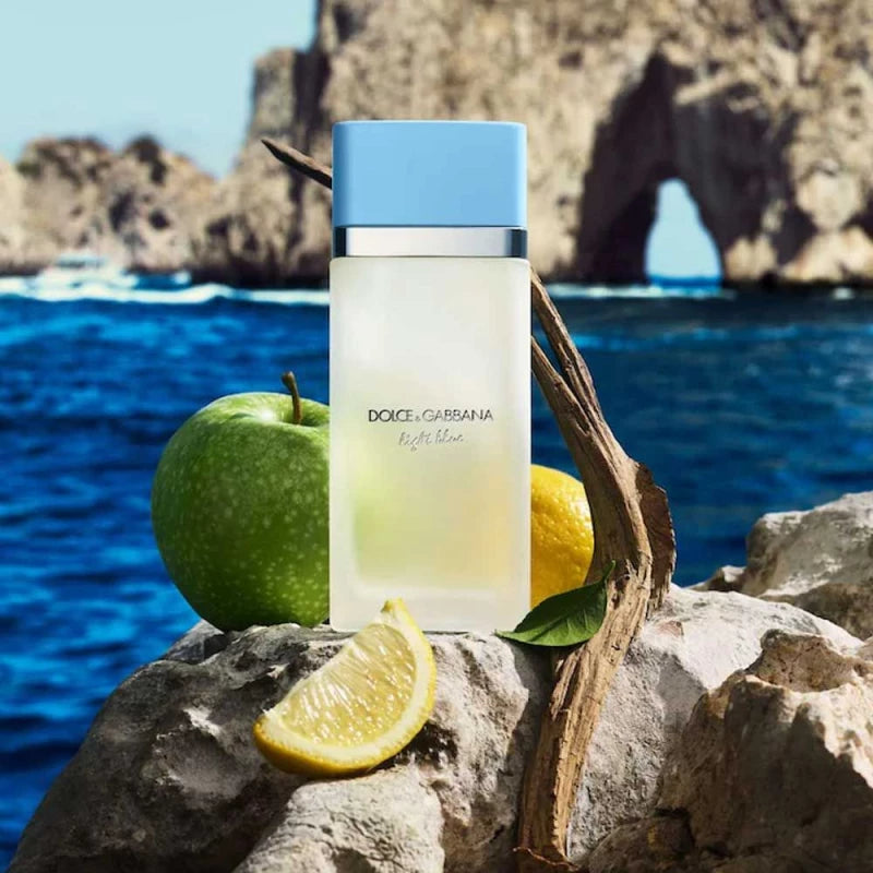 Dolce & Gabbana perfume bottle with an apple and lemon on rocks by the sea