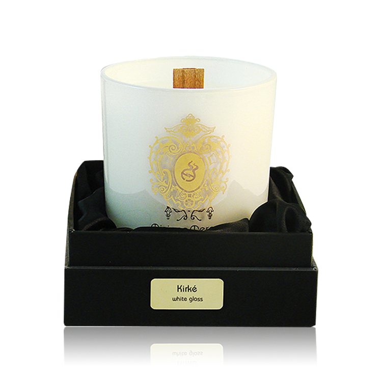 A white glass candle with a gold crest design and a wooden wick, presented in a black box with a gold label reading 'Kirké white gloss'.