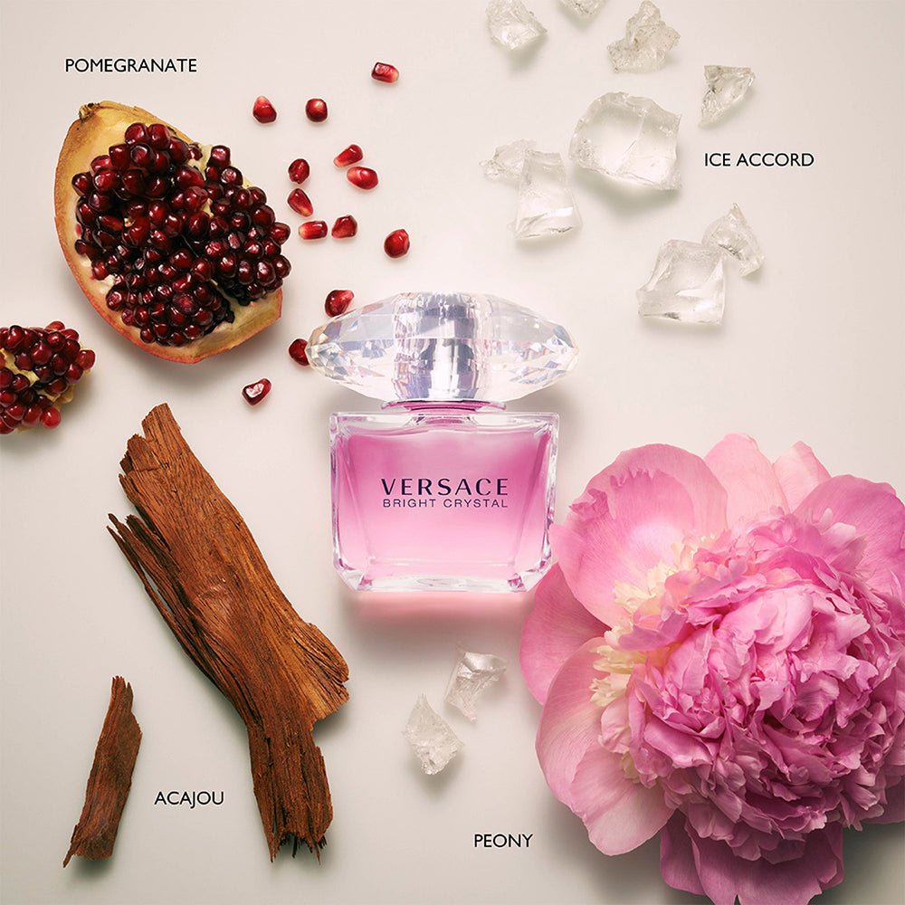 Versace Bright Crystal perfume bottle with pomegranate, ice cubes, cinnamon, and pink flower on a light background