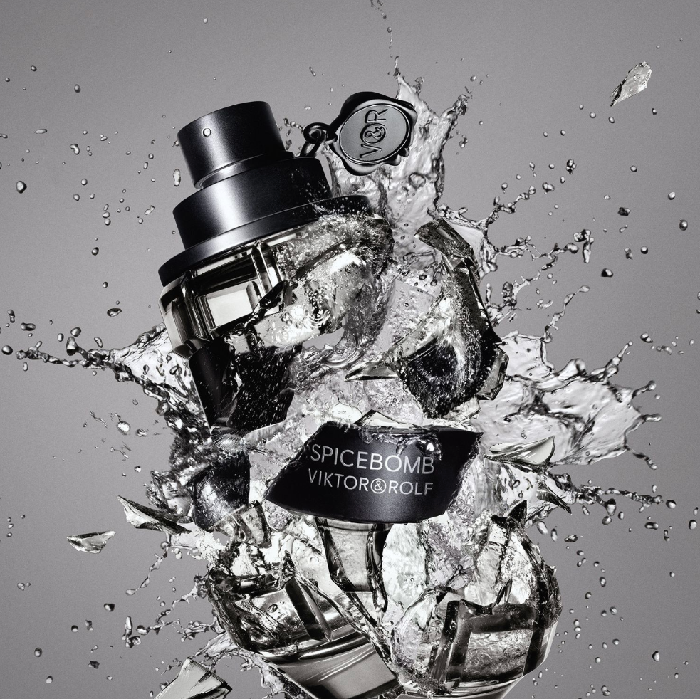 A Viktor & Rolf Spicebomb perfume bottle in black glass, dramatically bursting through ice cubes against a gray background with water splashes.