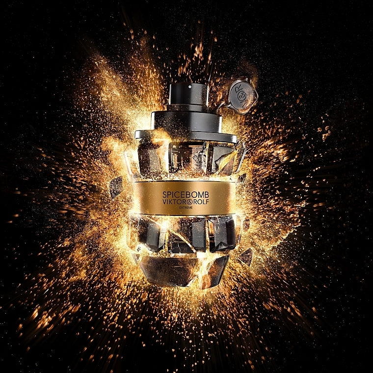 A bottle of Viktor & Rolf Spicebomb perfume centered against a black background with dramatic golden sparks and shattered-glass effects. The bottle is metallic gold and black with visible branding and the text 'SPICEBOMB VIKTOR & ROLF' on the front.